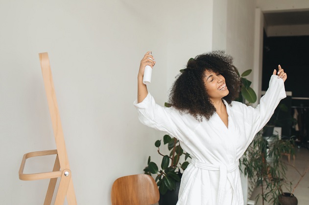 picture of a woman in a bathrobe in front a mirror putting a spray on her curly hair
